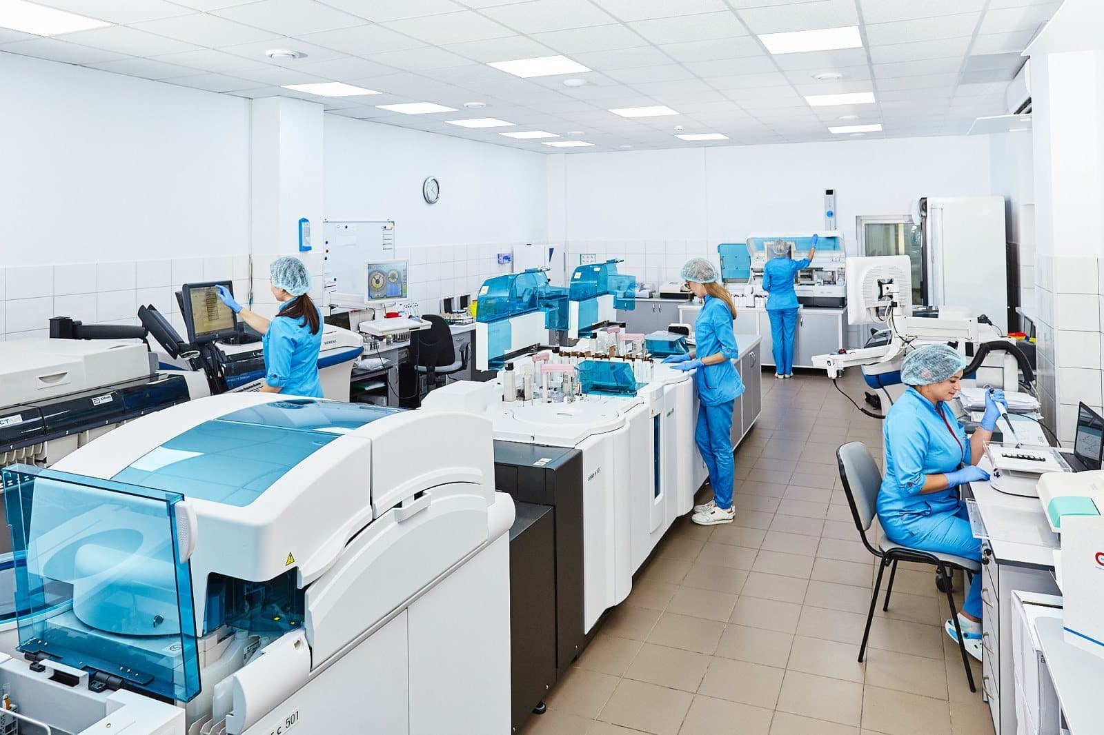 A working clinical laboratory with technicians at multiple analyser stations